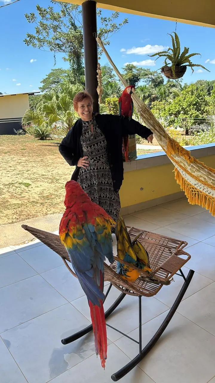 Sita Madhu com duas araras coloridas em um terraço